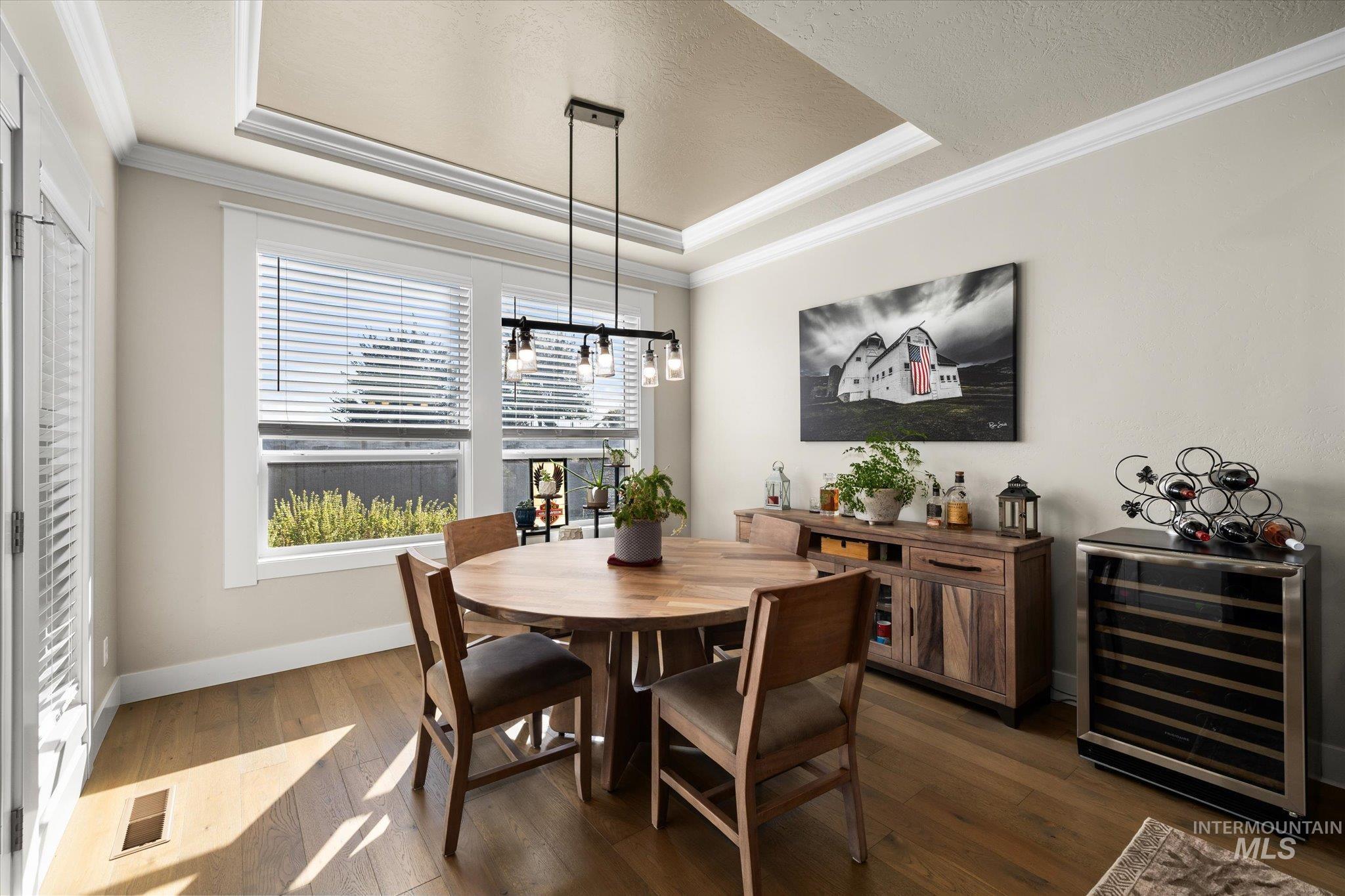 Dining space with a tray ceiling, wine cooler, crown molding, dark wood-style flooring, and a textured ceiling