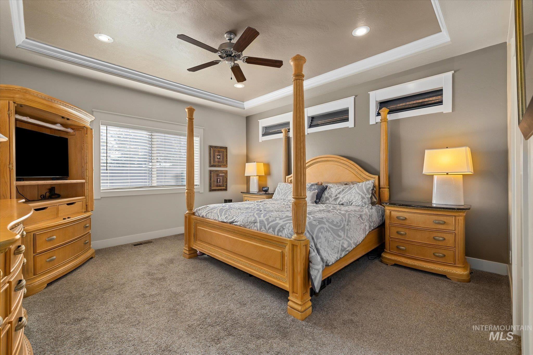 Carpeted bedroom with a raised ceiling, ceiling fan, and recessed lighting