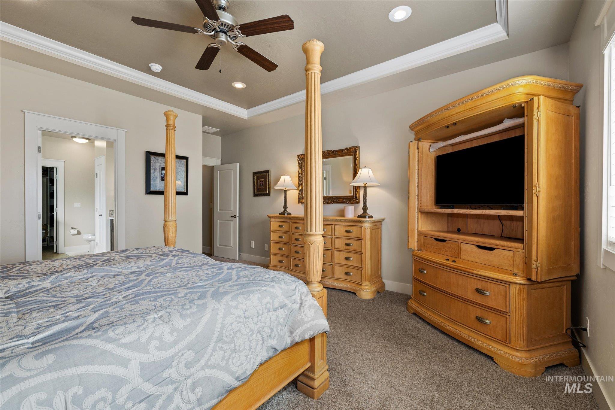 Carpeted bedroom with a tray ceiling, recessed lighting, ceiling fan, and crown molding