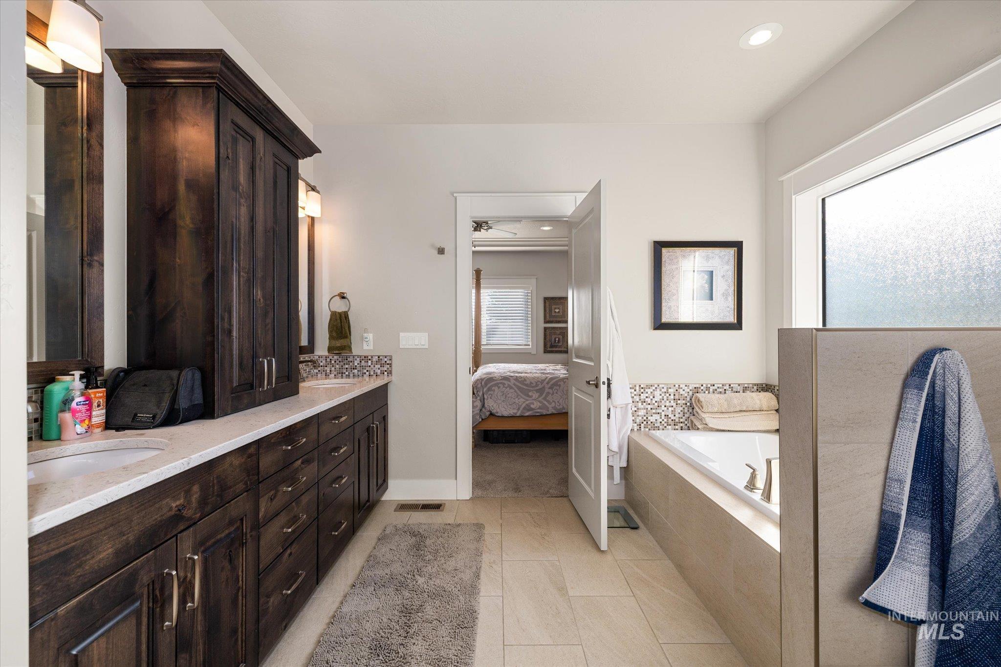 Full bath with ensuite bathroom, double vanity, a garden tub, recessed lighting, and light tile patterned floors