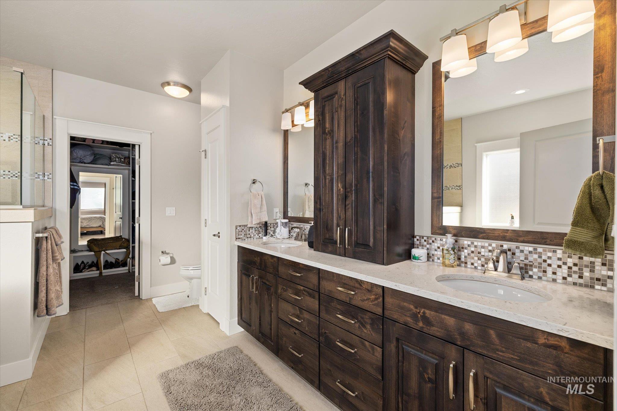 Bathroom featuring tasteful backsplash, double vanity, and light tile patterned floors