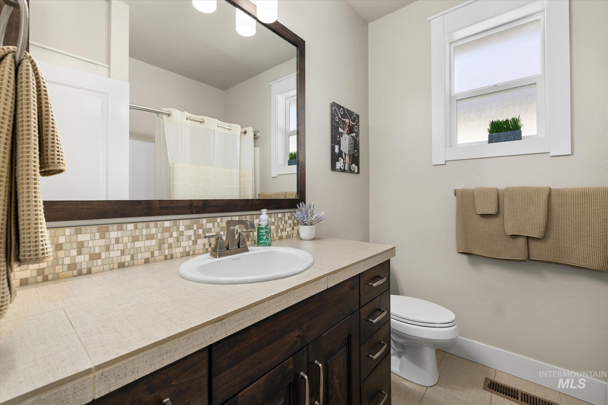Full bath with curtained shower, vanity, tasteful backsplash, and light tile patterned floors