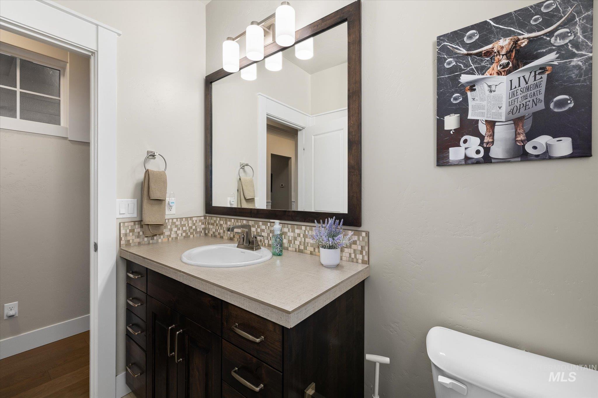 Half bath with decorative backsplash, vanity, and wood finished floors