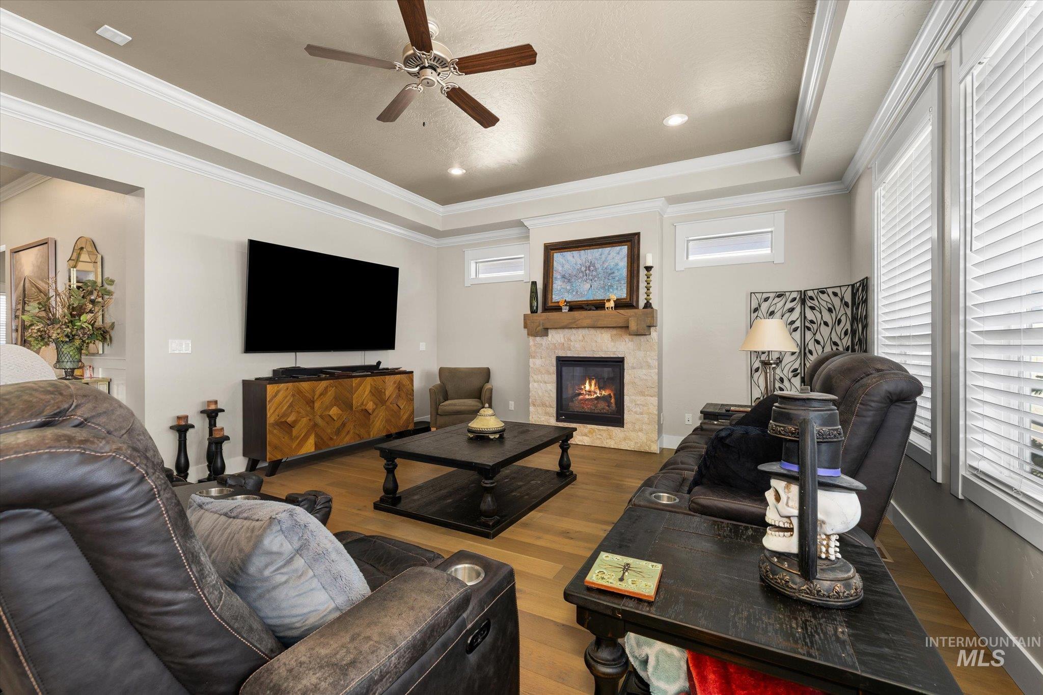Living room featuring a raised ceiling, healthy amount of natural light, wood finished floors, ornamental molding, and recessed lighting