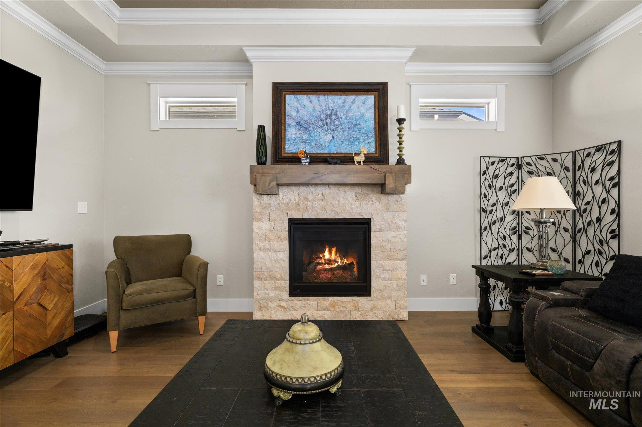 Living room with healthy amount of natural light, wood finished floors, a fireplace, crown molding, and a tray ceiling