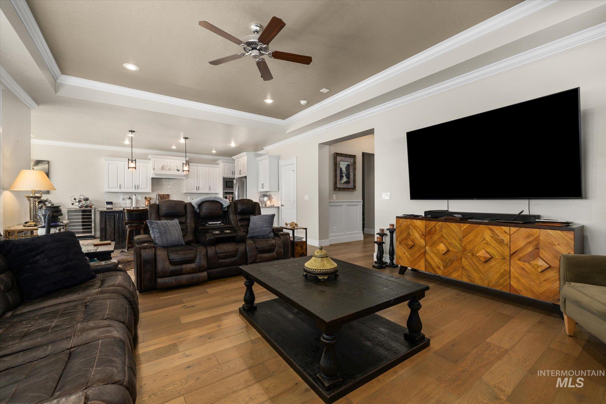 Living room featuring a tray ceiling, crown molding, dark wood-style floors, a ceiling fan, and recessed lighting