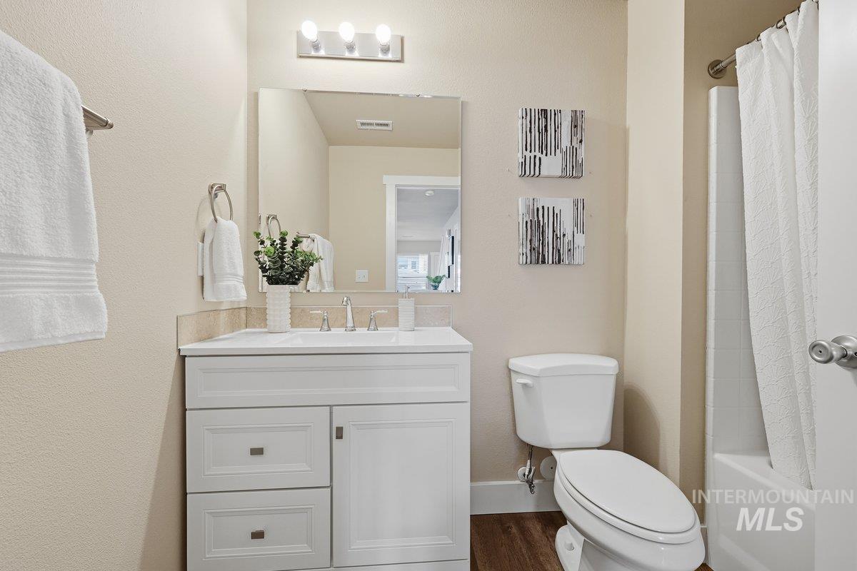 Bathroom featuring vanity, shower / bath combination with curtain, and dark wood-type flooring