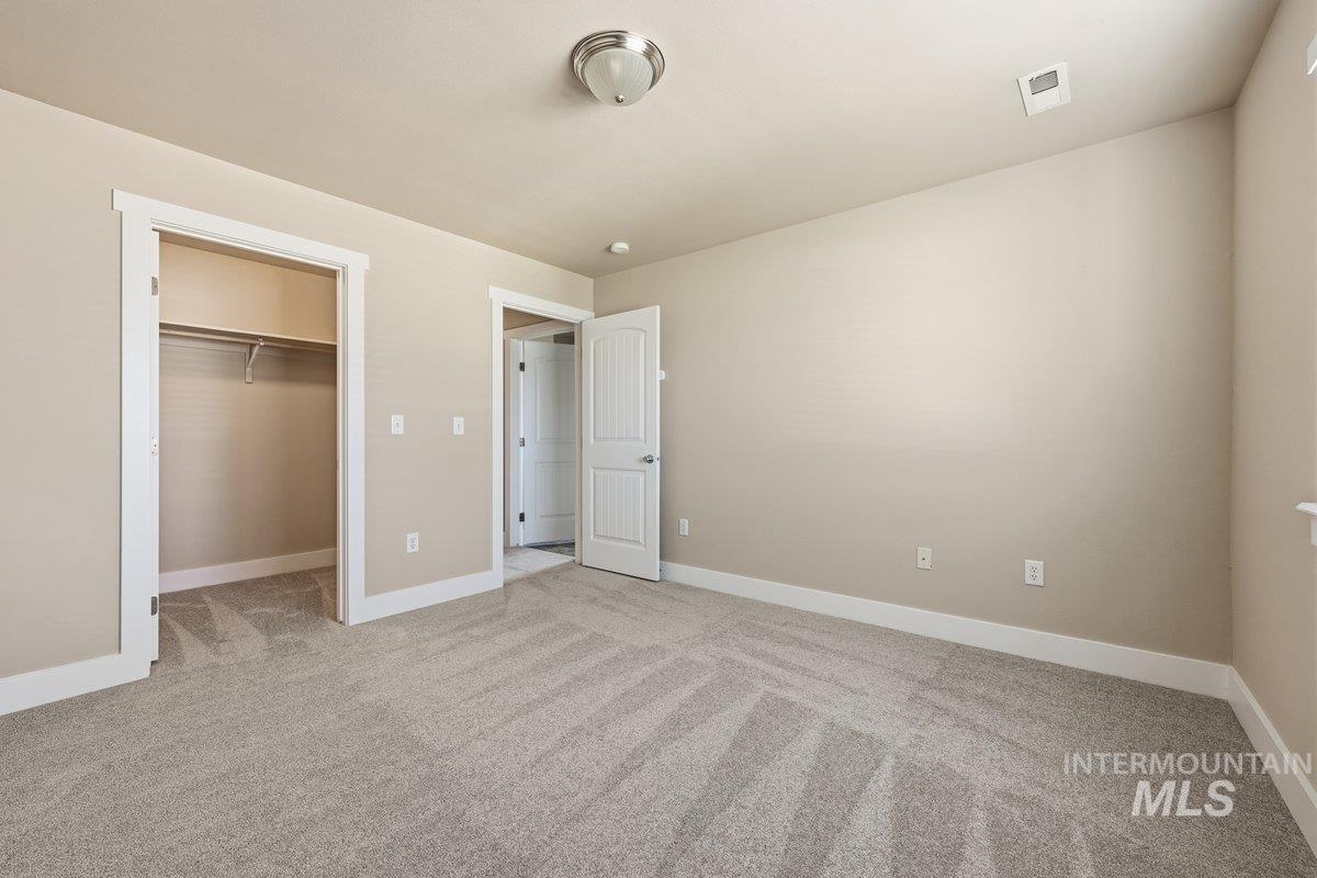 Unfurnished bedroom featuring a walk in closet and light carpet