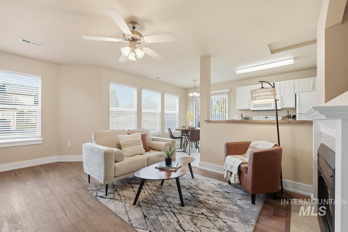 Living room featuring ceiling fan, light wood-style flooring, a fireplace, and a chandelier