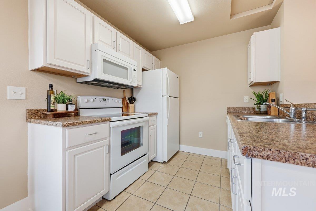 Kitchen featuring white appliances, white cabinetry, light tile patterned flooring, and dark countertops