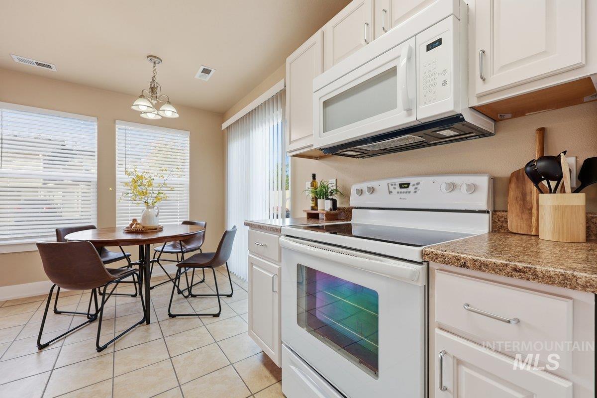 Kitchen featuring white appliances, white cabinetry, pendant lighting, light tile patterned floors, and a chandelier