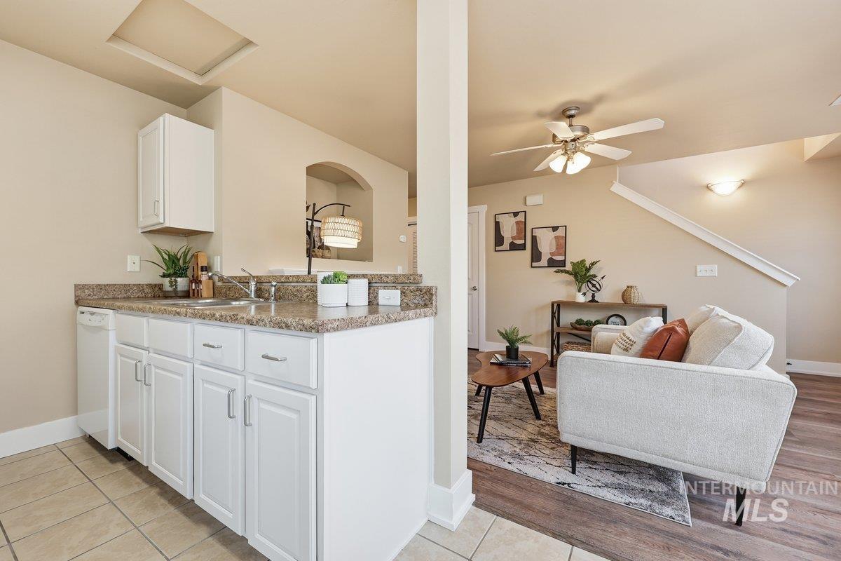 Kitchen featuring white cabinetry, white dishwasher, a peninsula, open floor plan, and light stone counters