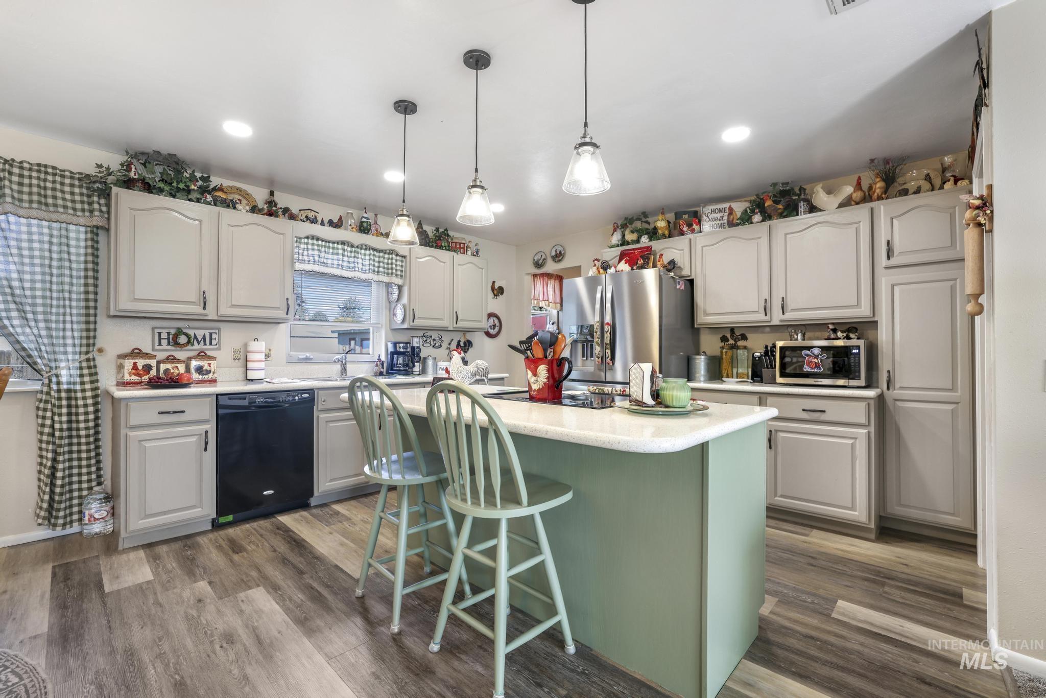 Kitchen featuring pendant lighting, a kitchen breakfast bar, light countertops, appliances with stainless steel finishes, and dark wood-type flooring