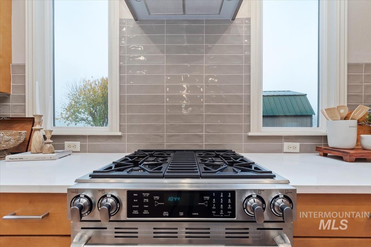Kitchen view of light countertops, stainless steel range, tasteful backsplash, and extractor fan