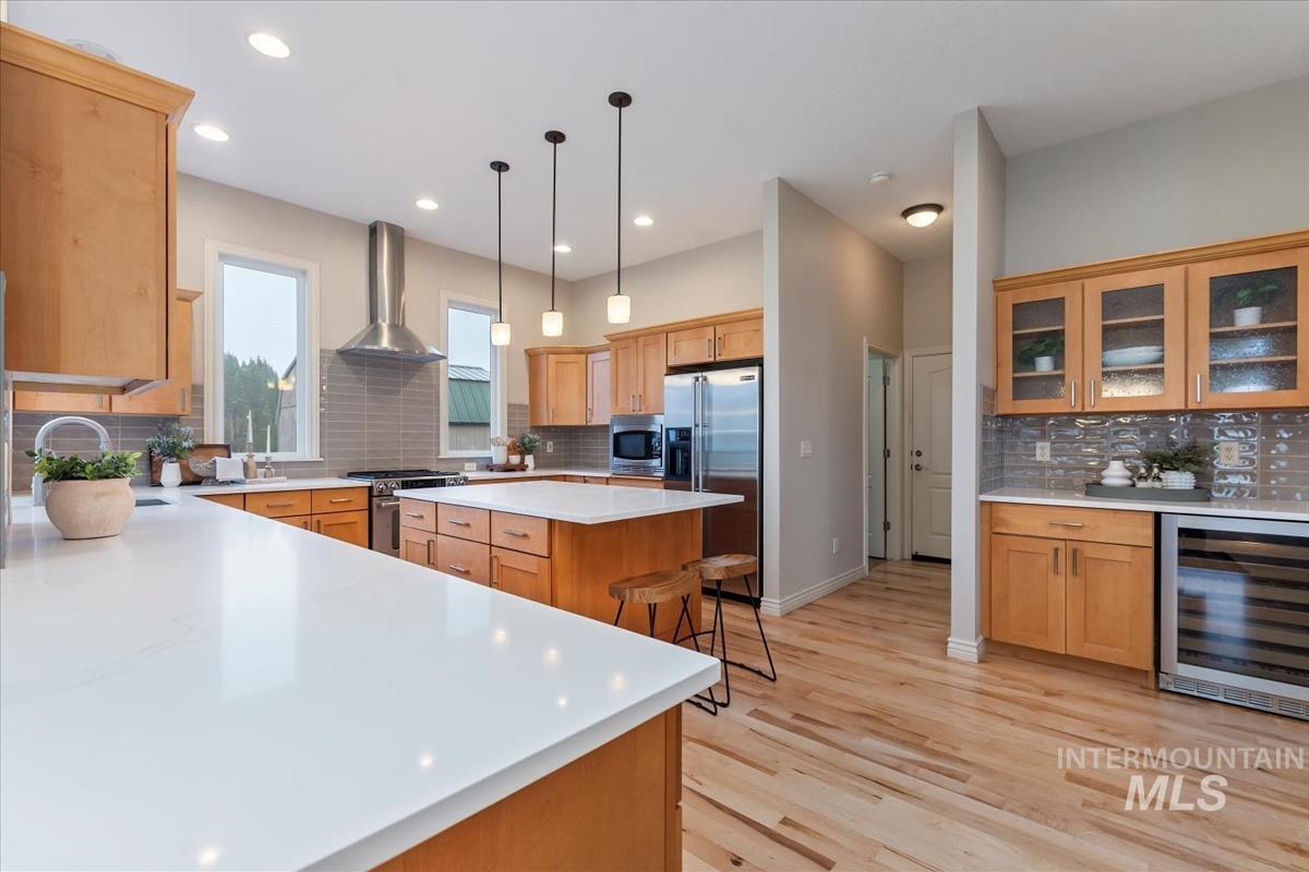 Kitchen featuring backsplash, beverage cooler, stainless steel appliances, decorative light fixtures, and recessed lighting