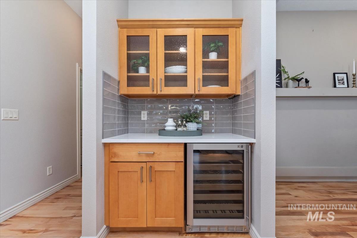 Bar area with tasteful backsplash, wine cooler, glass insert cabinets, and light wood finished floors