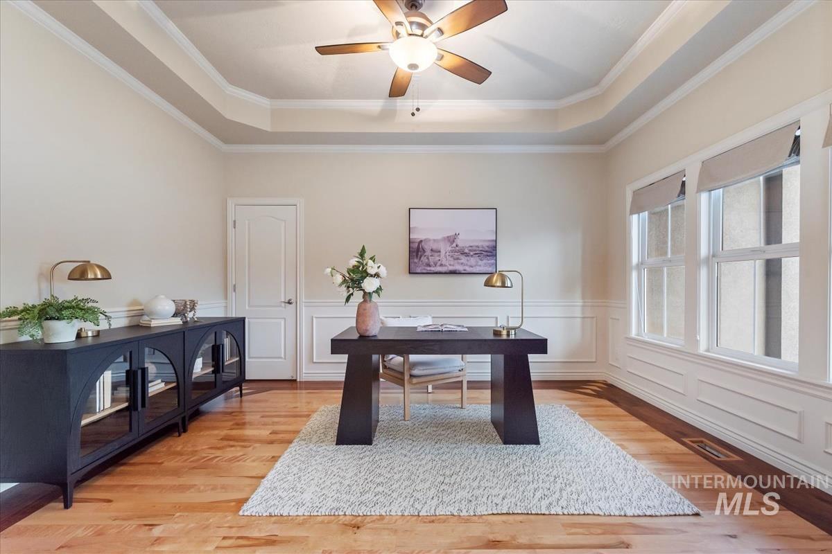 Office space with a tray ceiling, a wainscoted wall, a decorative wall, light wood-style flooring, and crown molding