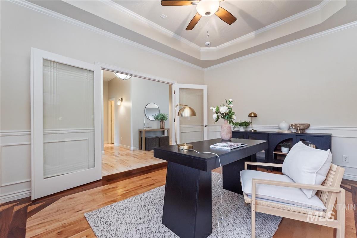 Home office with a raised ceiling, light wood-type flooring, crown molding, a ceiling fan, and a decorative wall