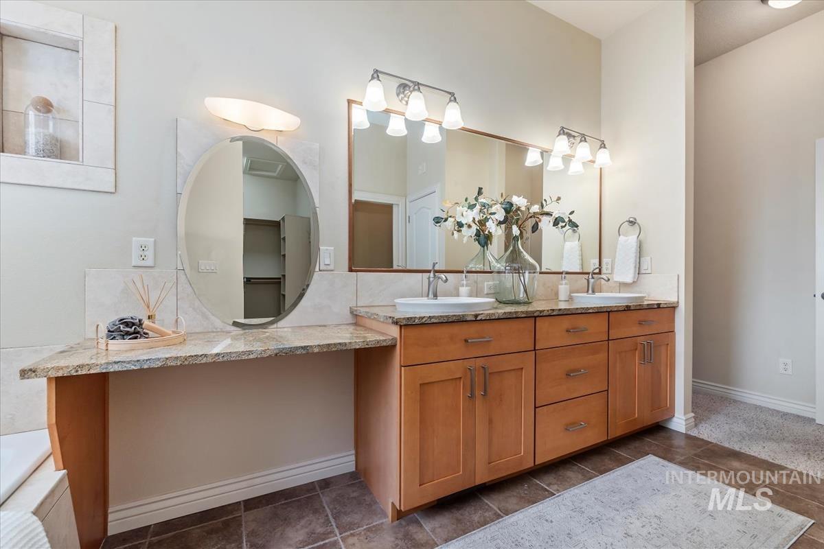 Full bathroom with double vanity, dark tile patterned flooring, and a tub to relax in