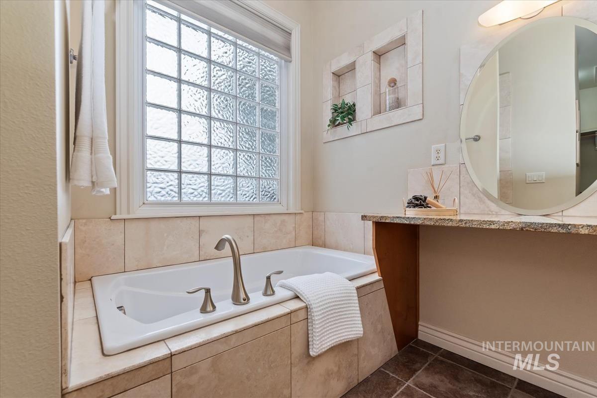 Full bathroom featuring a garden tub and dark tile patterned flooring