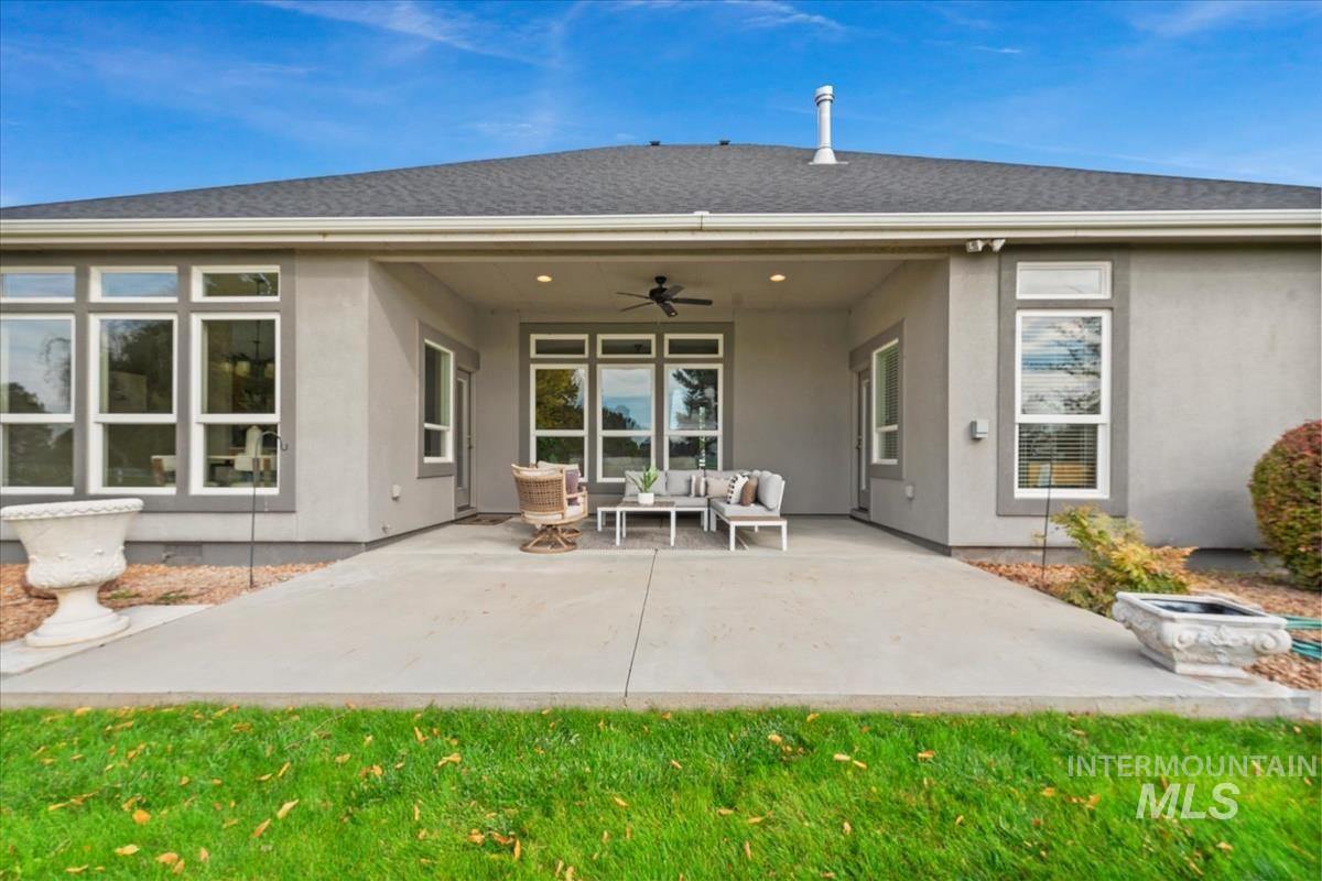 Rear view of property with a ceiling fan, an outdoor living space, a patio area, stucco siding, and a lawn
