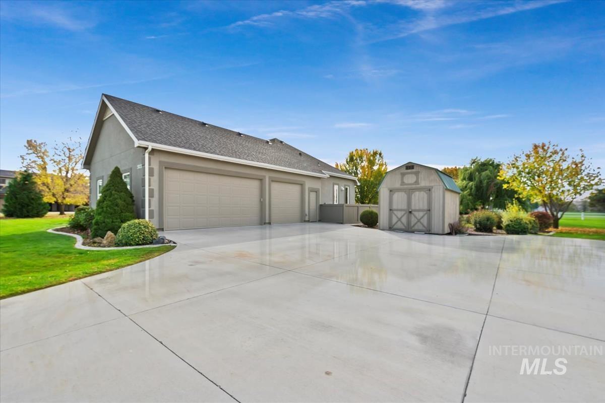 View of home's exterior featuring a storage unit, concrete driveway, a yard, stucco siding, and a shingled roof