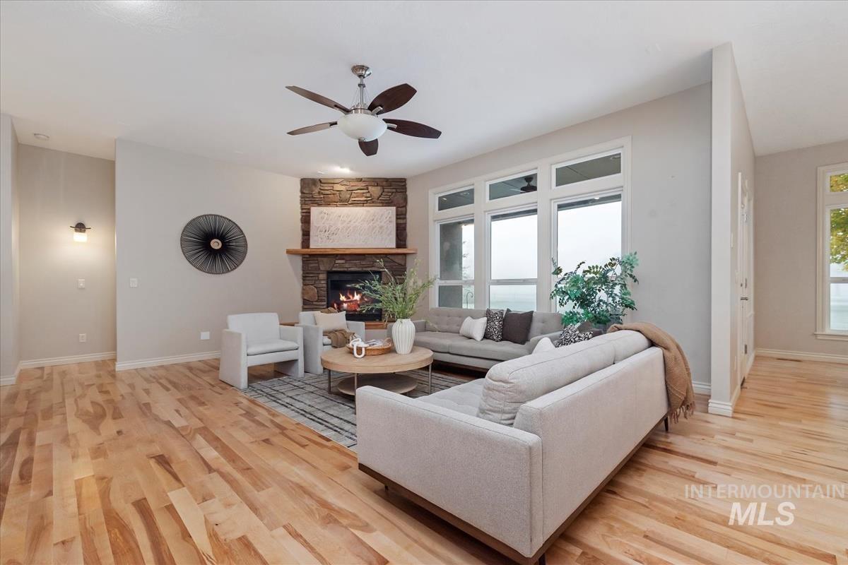 Living room featuring a ceiling fan, a stone fireplace, and light wood-type flooring