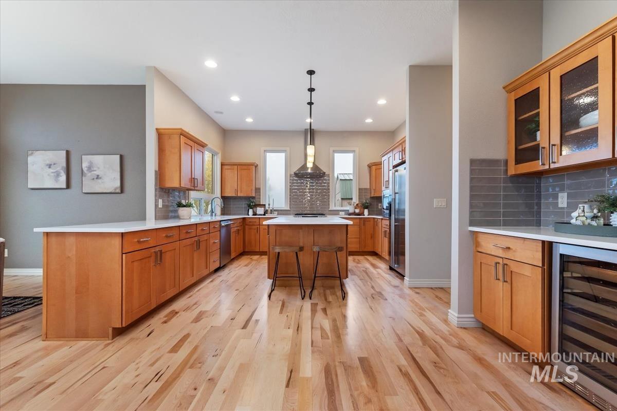 Kitchen featuring a breakfast bar, wine cooler, brown cabinetry, decorative light fixtures, and glass insert cabinets