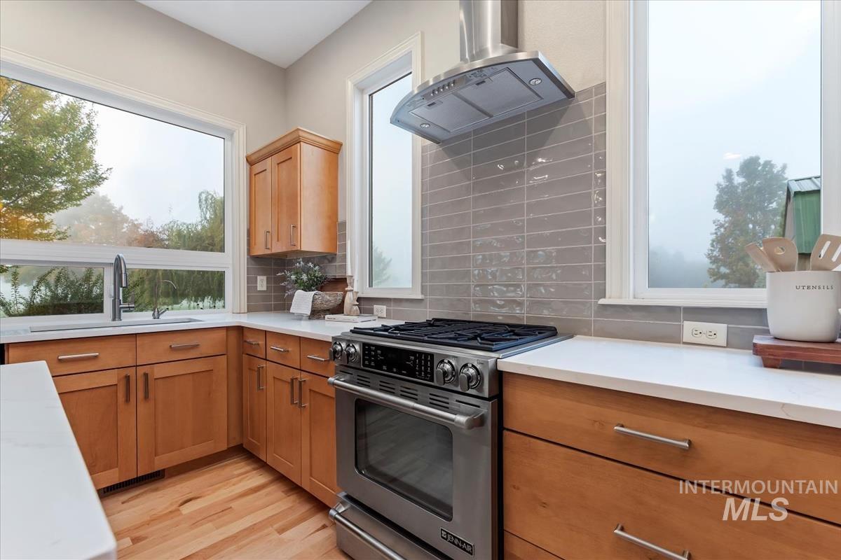 Kitchen with stainless steel range, range hood, decorative backsplash, light wood-style floors, and brown cabinets
