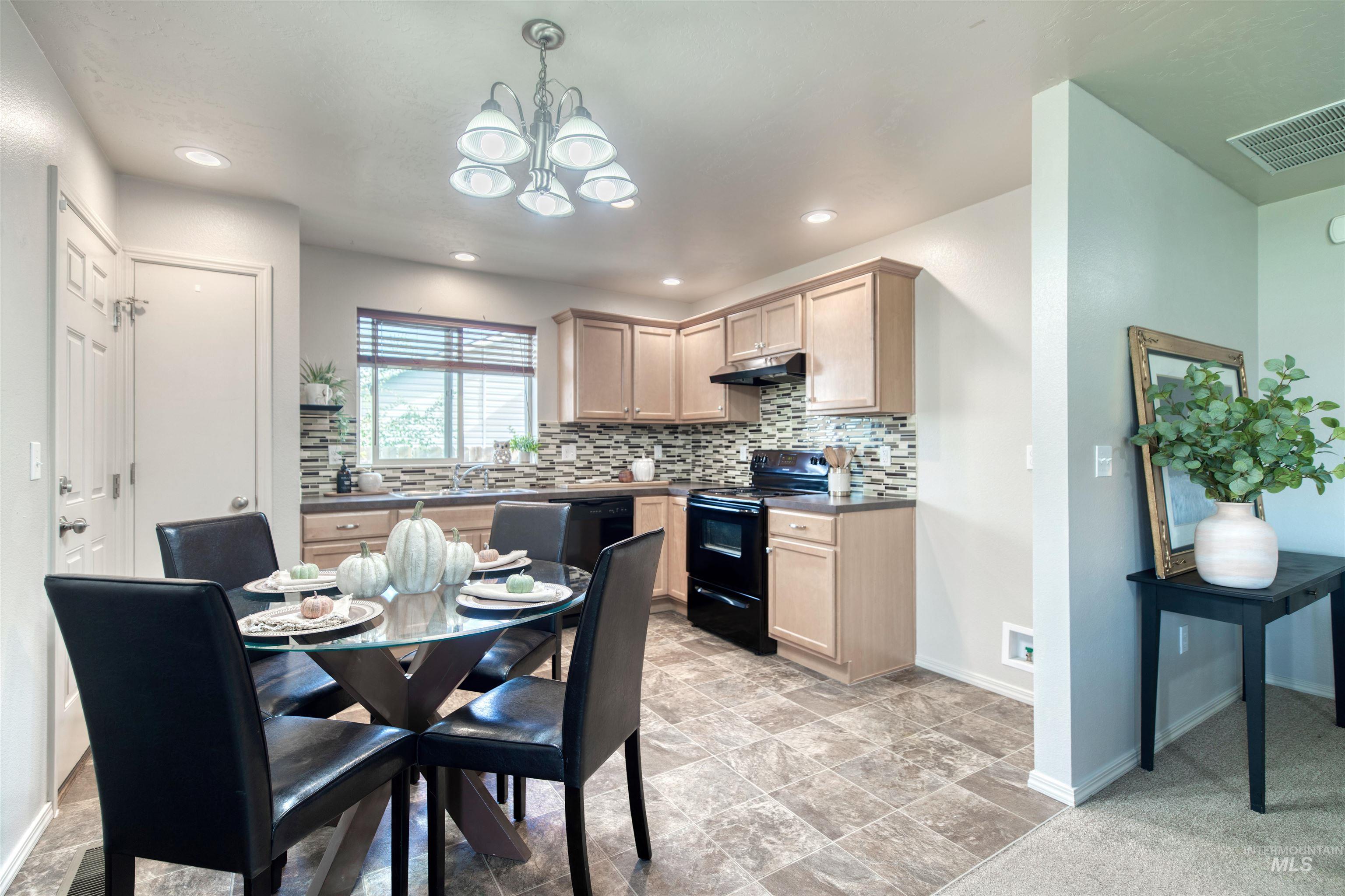 Kitchen with black electric range, backsplash, pendant lighting, a chandelier, and dark countertops