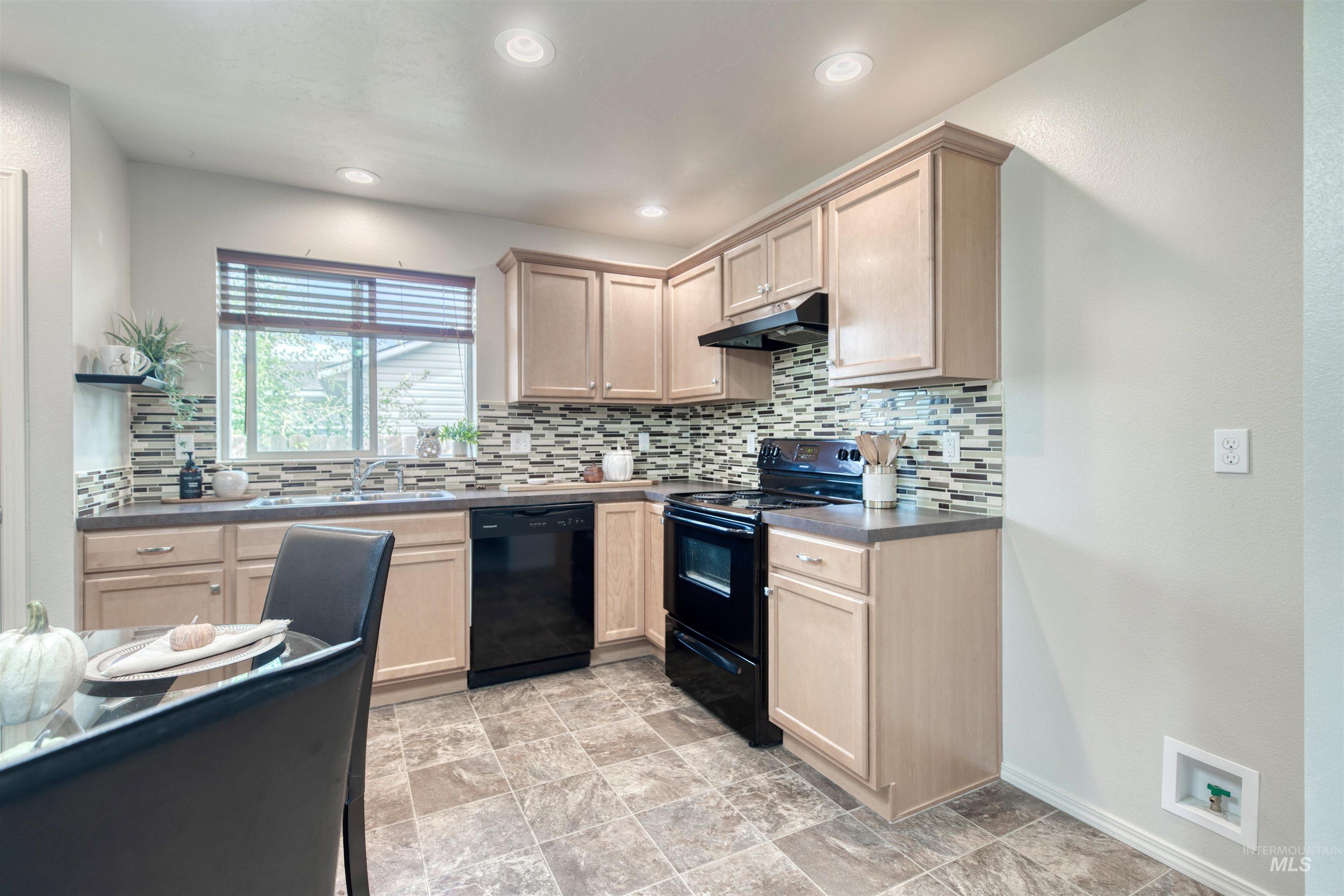 Kitchen with tasteful backsplash, black appliances, light brown cabinets, dark countertops, and under cabinet range hood