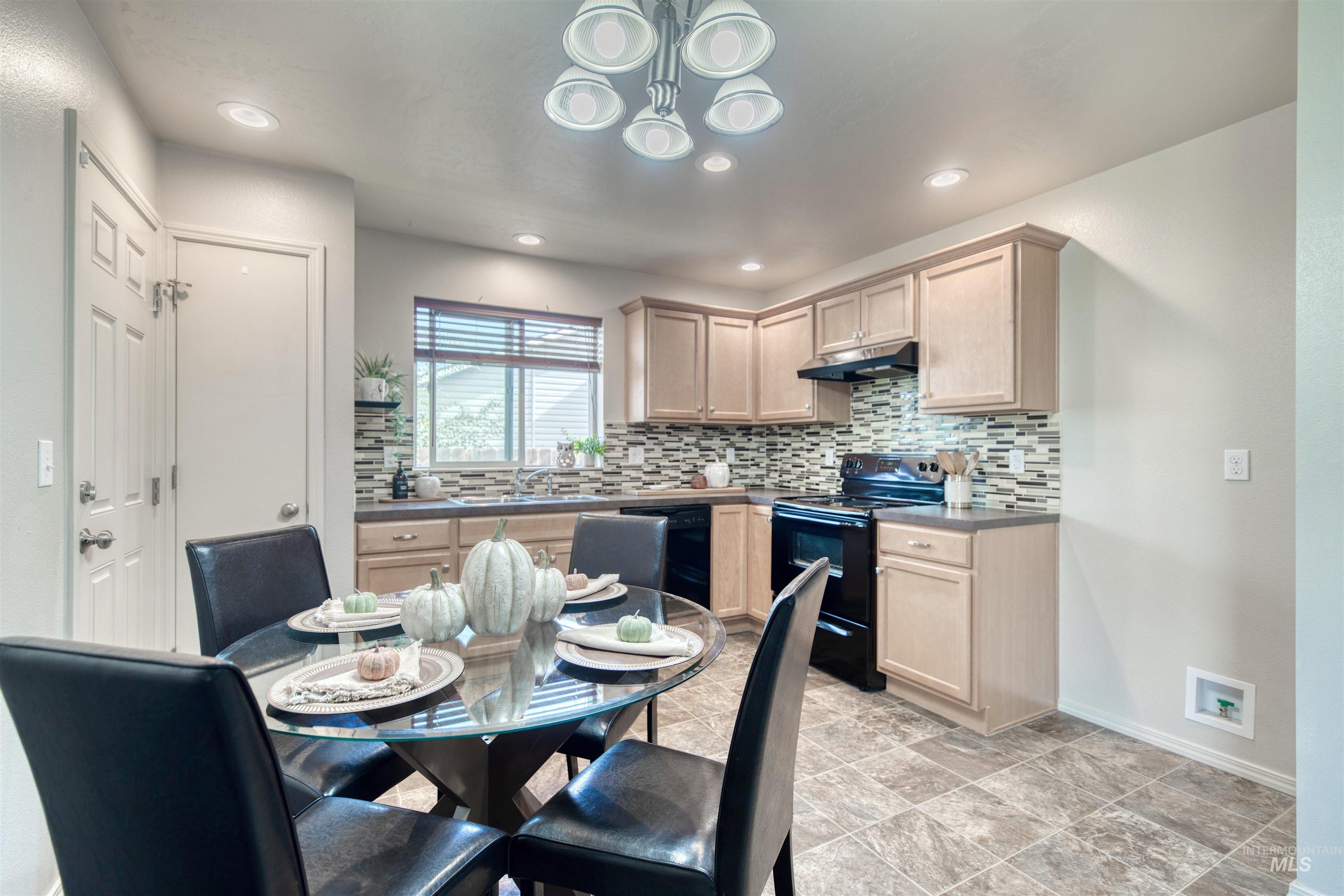 Kitchen with tasteful backsplash, black appliances, light brown cabinetry, dark countertops, and under cabinet range hood