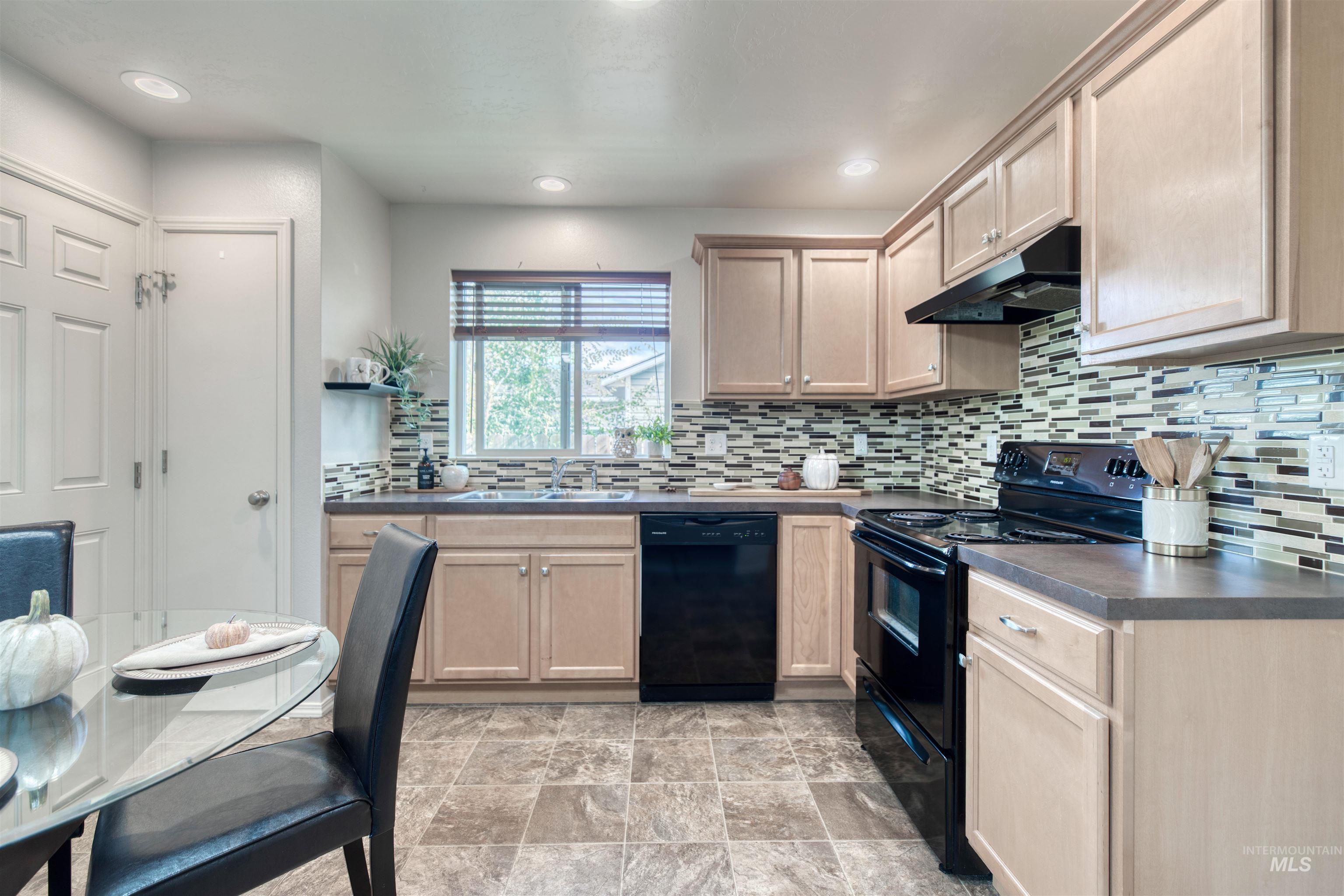Kitchen with black appliances, dark countertops, tasteful backsplash, under cabinet range hood, and light brown cabinets