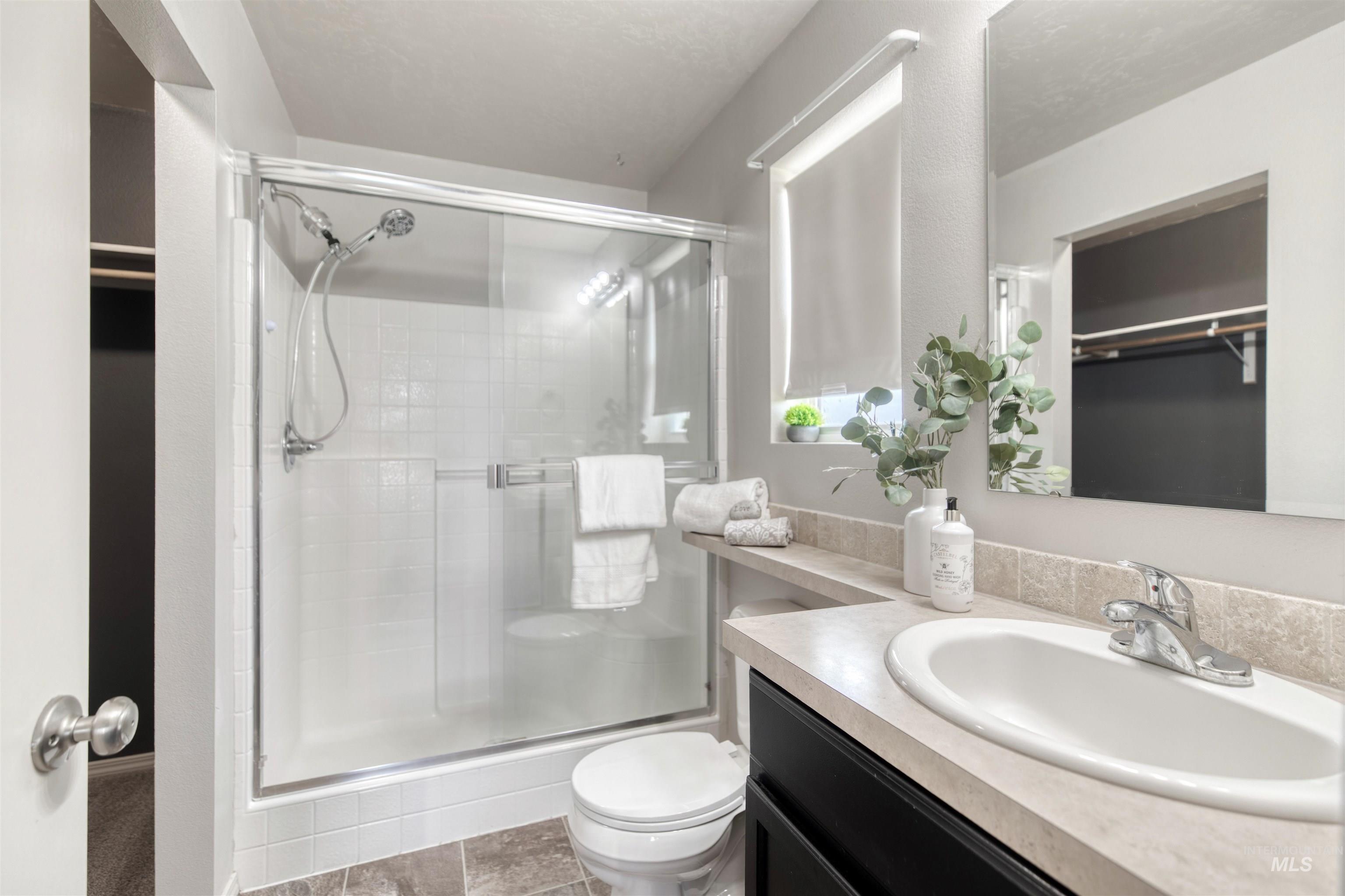 Full bathroom with a spacious closet, vanity, a stall shower, and light tile patterned floors