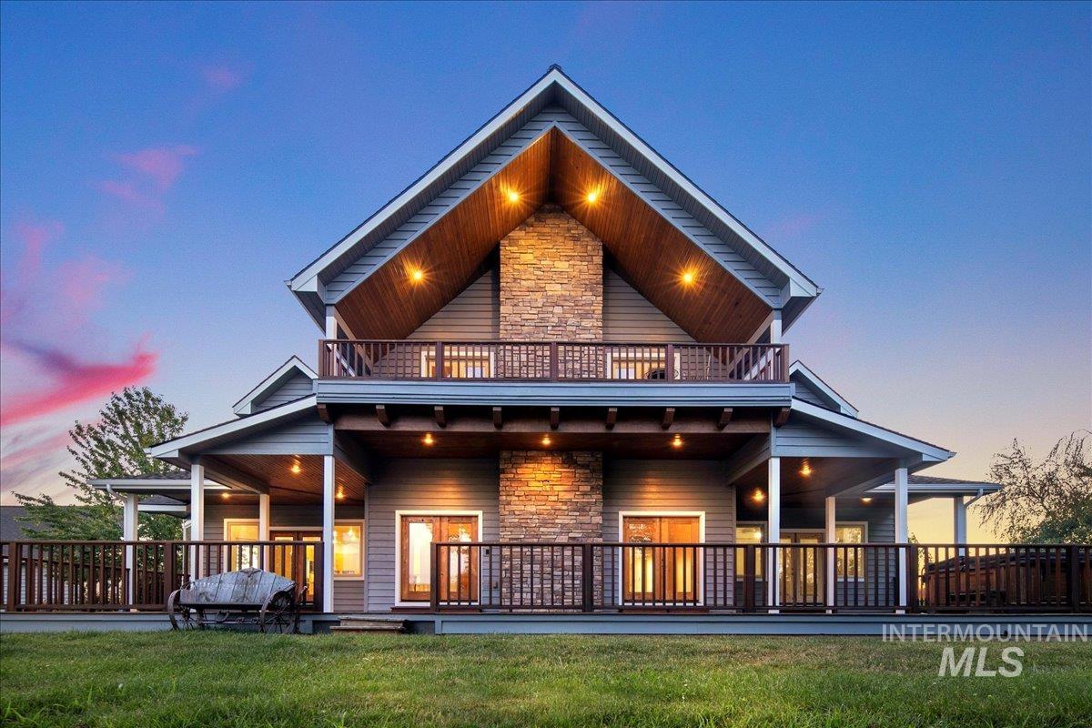 Back of property at dusk featuring a balcony, stone siding, and a yard