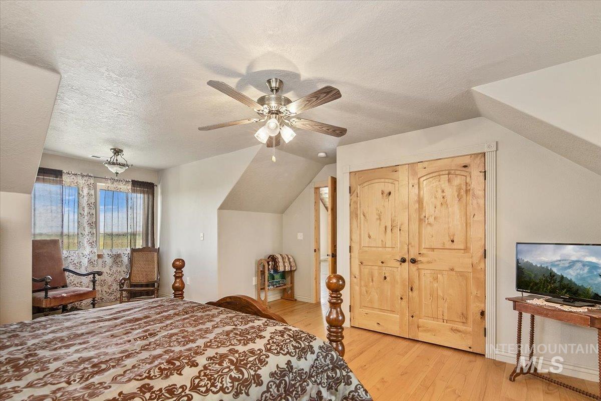 Bedroom with light wood-style floors, a textured ceiling, vaulted ceiling, and ceiling fan