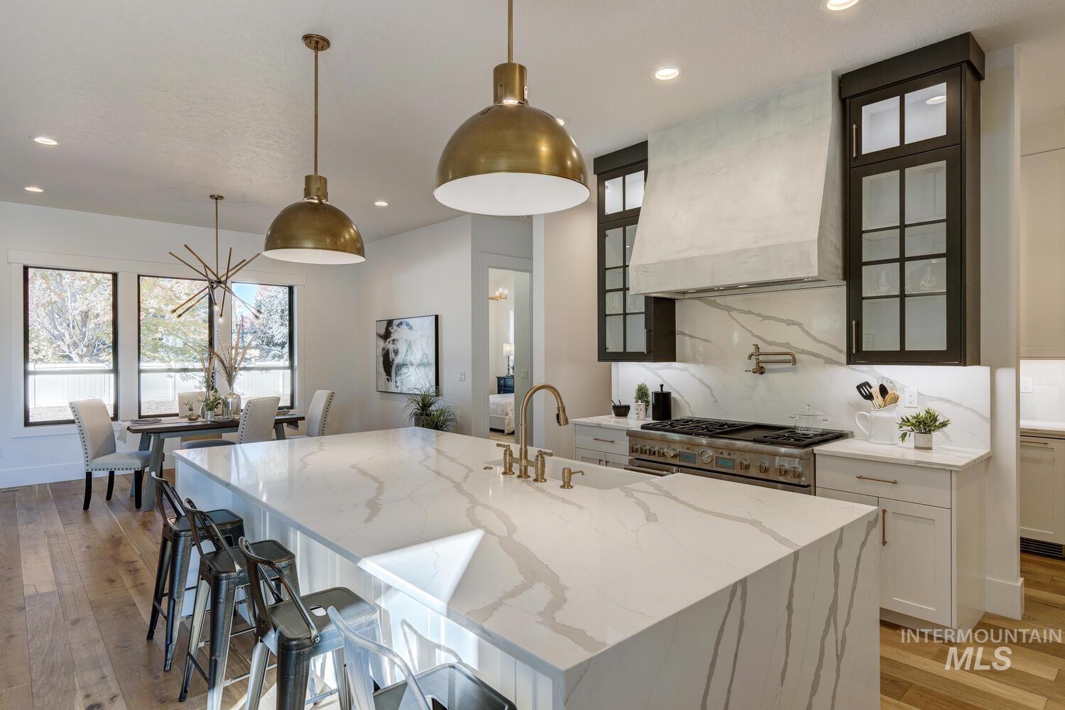 Kitchen with white cabinets, light wood finished floors, light stone counters, hanging light fixtures, and custom range hood