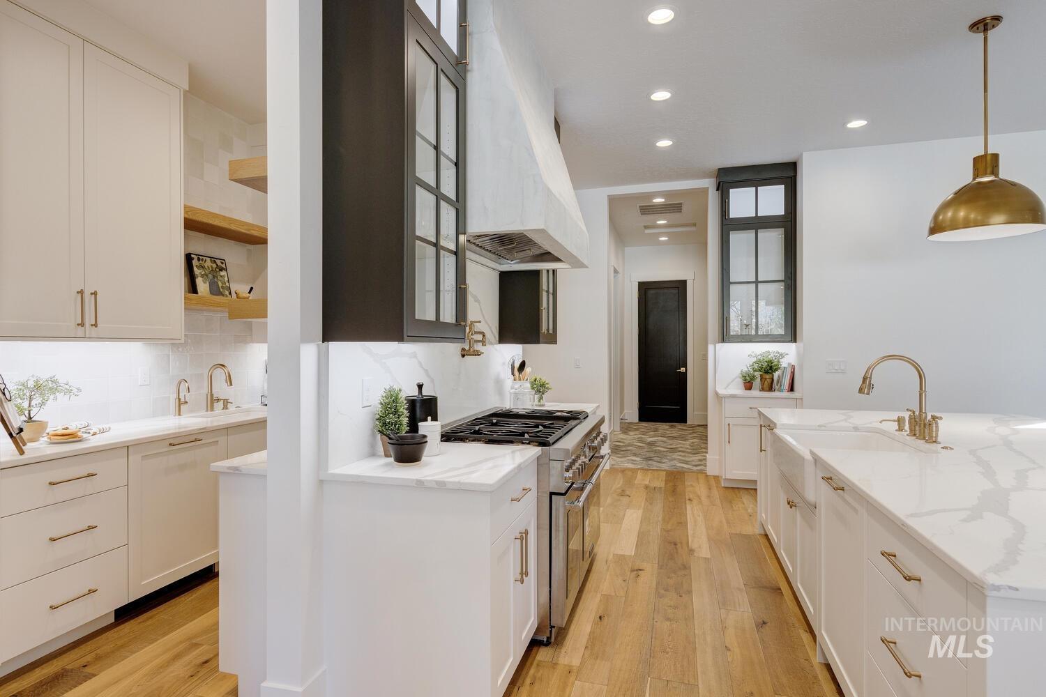 Kitchen with white cabinetry, range with two ovens, custom exhaust hood, hanging light fixtures, and light stone countertops