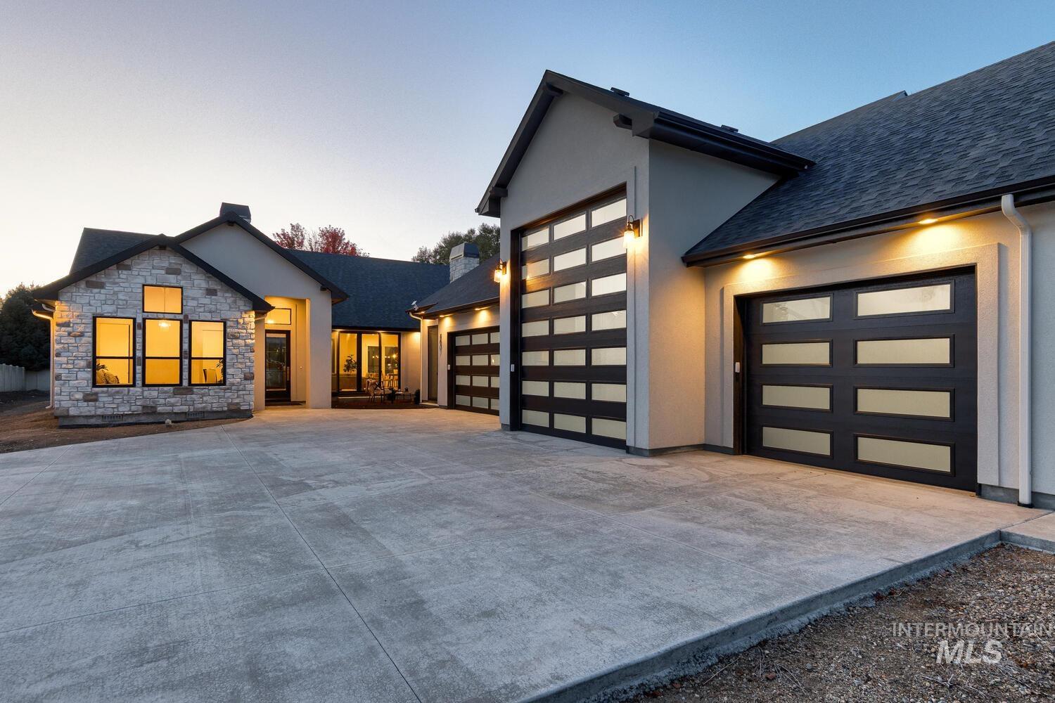 Exterior space featuring a garage, driveway, a shingled roof, stone siding, and stucco siding