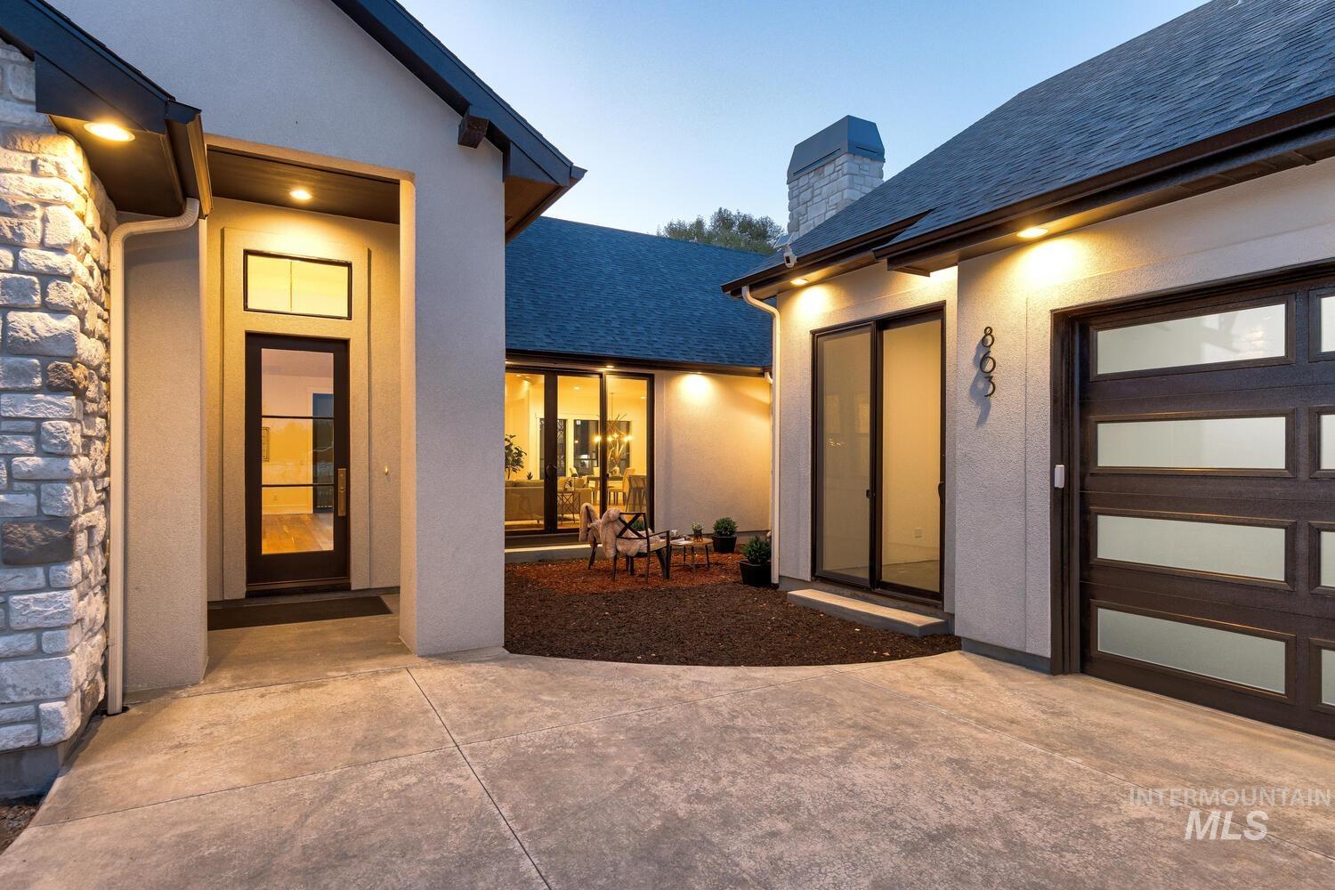 Exterior entry at dusk featuring a shingled roof, a chimney, and stucco siding