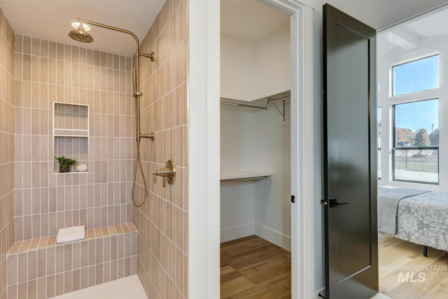 Ensuite bathroom featuring light wood finished floors, a walk in closet, and tiled shower