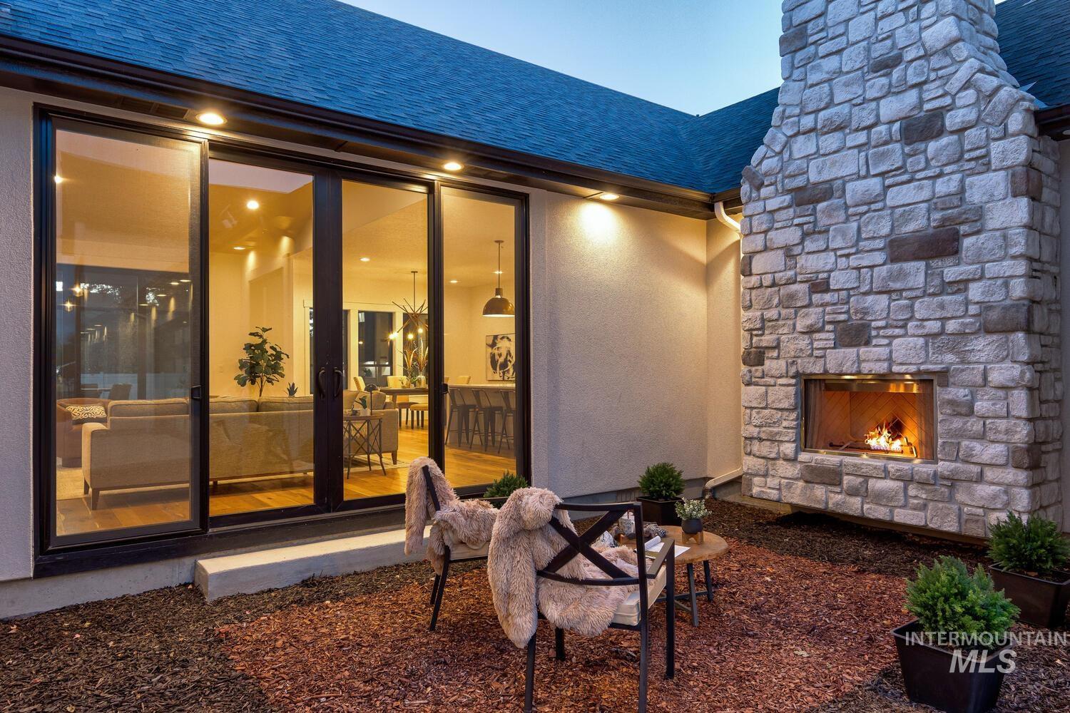 View of exterior entry with an outdoor stone fireplace, roof with shingles, stone siding, stucco siding, and a chimney