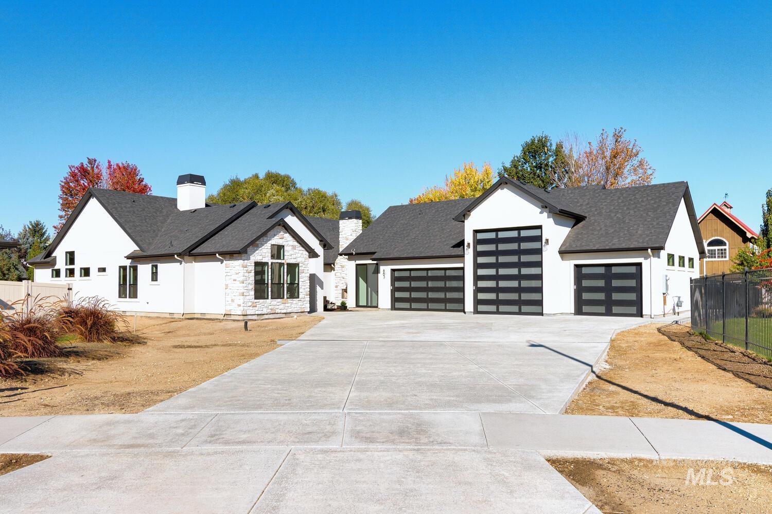 Modern inspired farmhouse with a garage, concrete driveway, a chimney, stone siding, and roof with shingles
