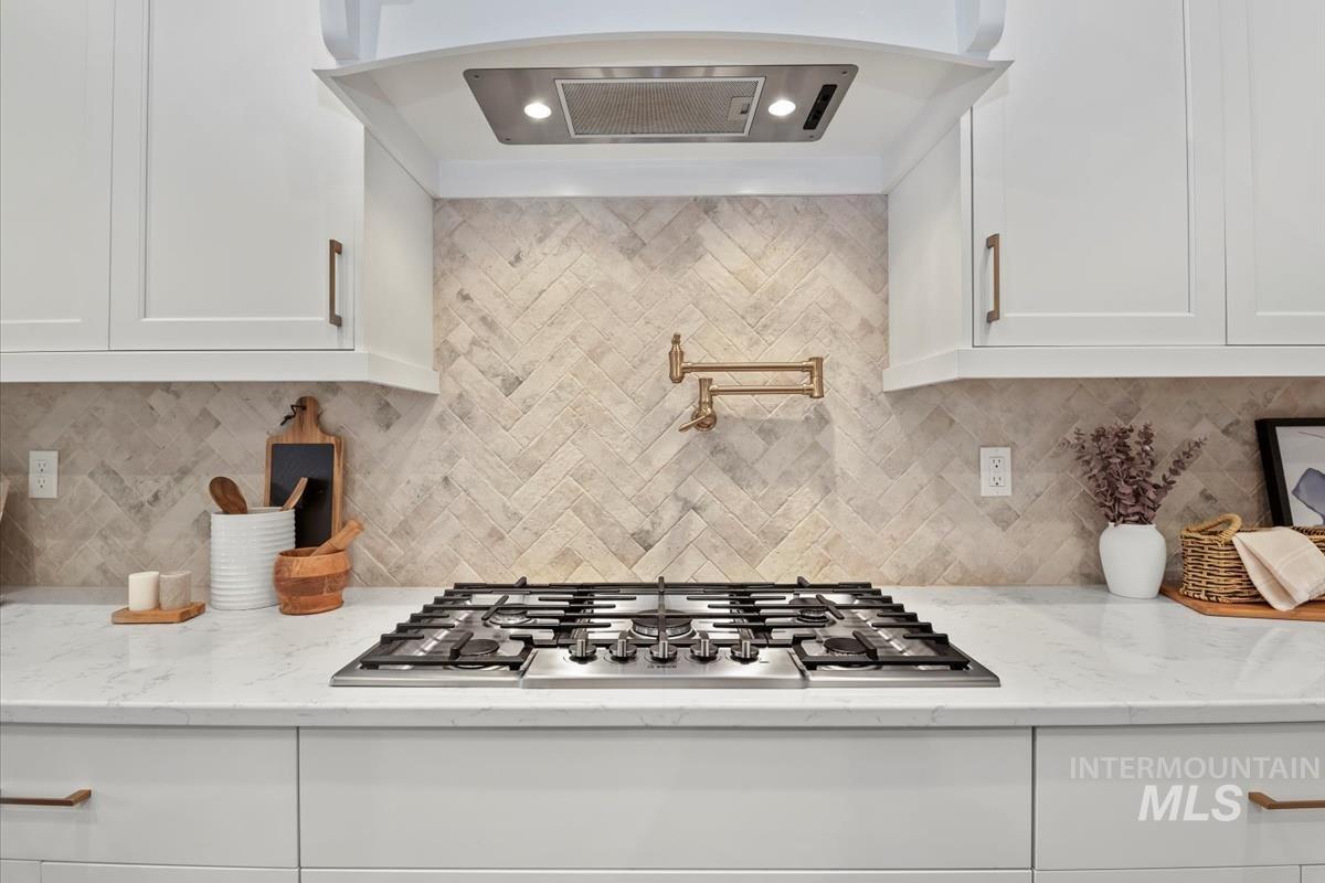 Kitchen with exhaust hood, tasteful backsplash, and white cabinets