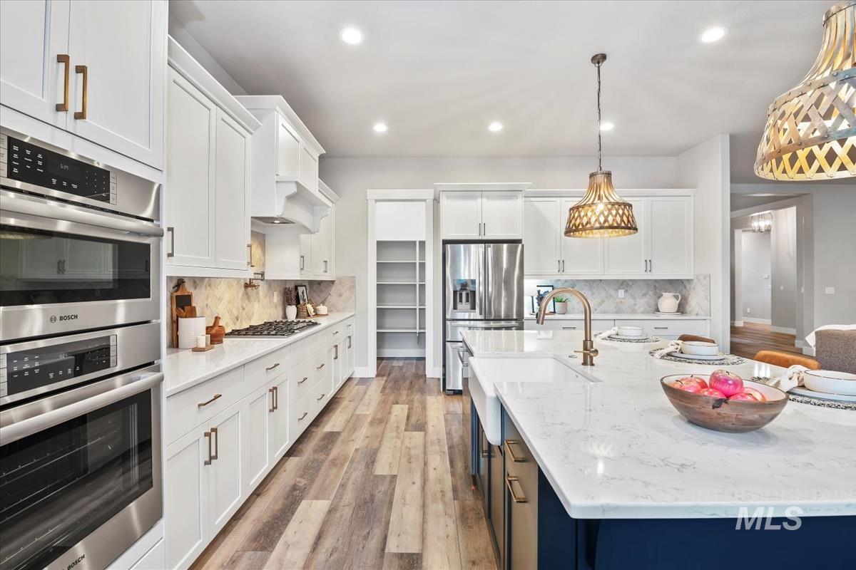 Kitchen featuring appliances with stainless steel finishes, white cabinetry, light stone countertops, light wood-type flooring, and recessed lighting