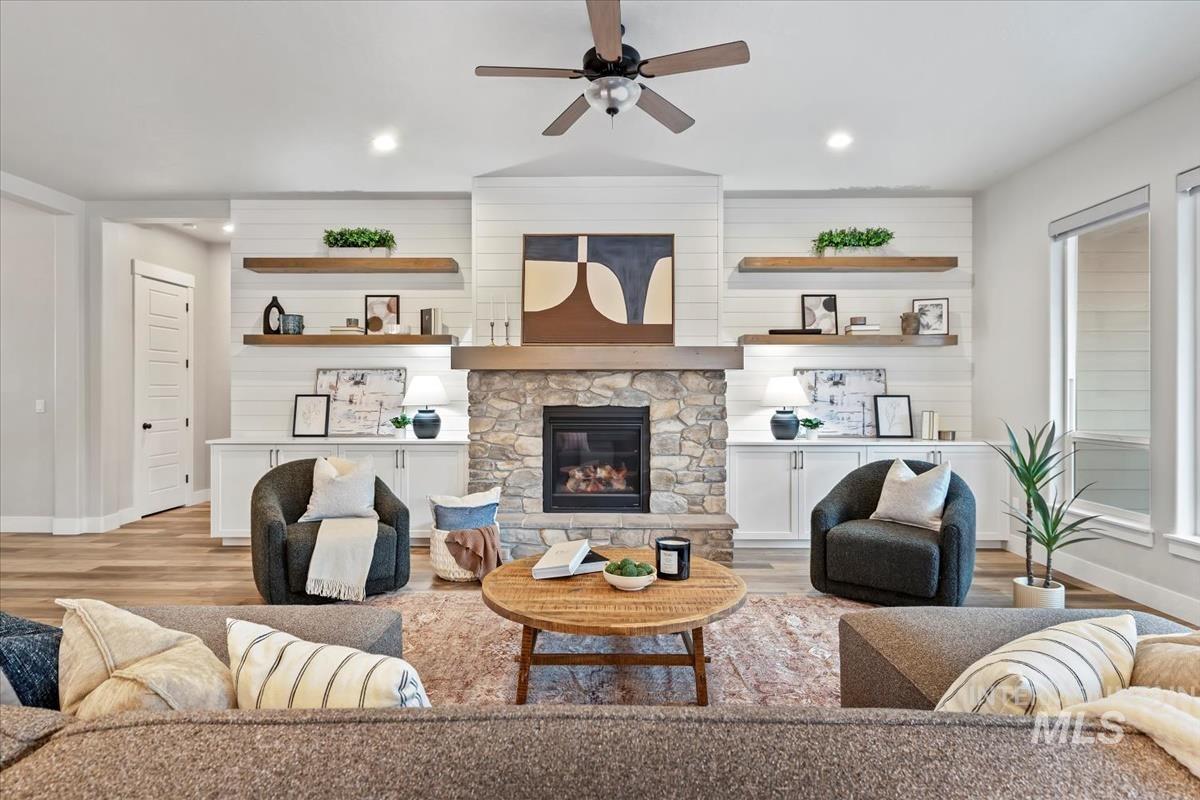 Living room with light wood finished floors, a stone fireplace, recessed lighting, a ceiling fan, and wood walls