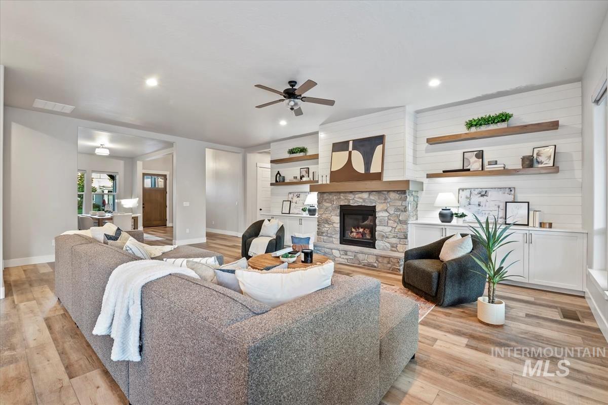 Living area with a stone fireplace, light wood-style flooring, a ceiling fan, and recessed lighting