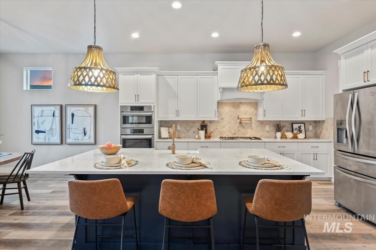 Kitchen with tasteful backsplash, light wood finished floors, white cabinets, appliances with stainless steel finishes, and light stone countertops