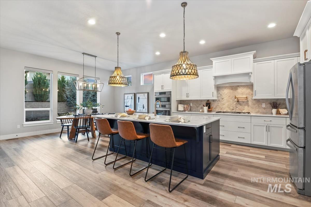 Kitchen with pendant lighting, white cabinets, backsplash, an island with sink, and recessed lighting