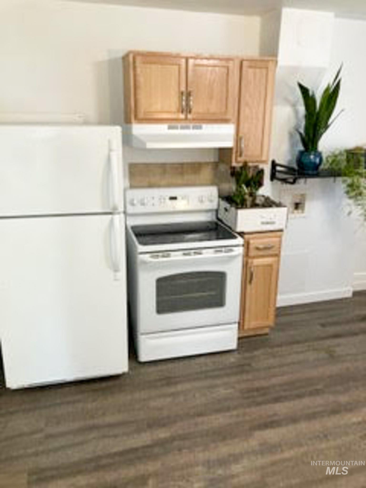 Kitchen featuring white appliances, dark wood-style flooring, under cabinet range hood, and light countertops